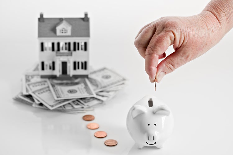 model house sits on top of money next to pifggy bank; mortgage concept